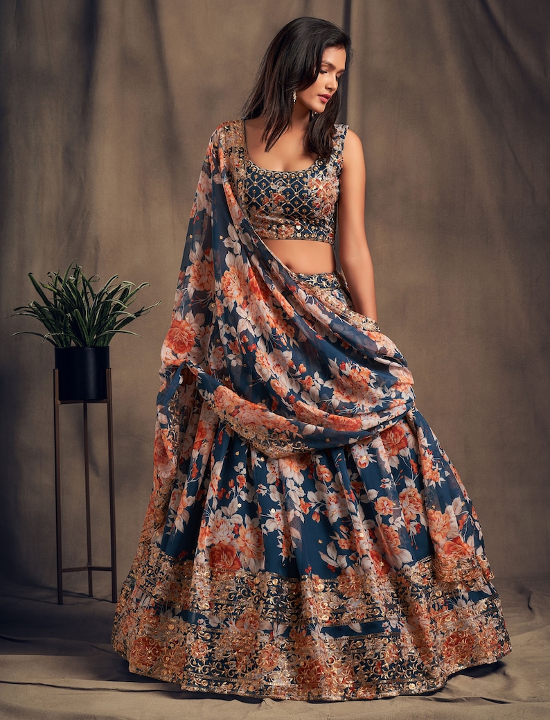 May include: A teal blue and orange floral print lehenga with a matching sleeveless crop top. The lehenga has a gold embroidered border and the crop top has gold embellishments.