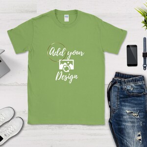 May include: A light green t-shirt with a white circle and the text "Add your Design" inside the circle. The circle has a gold outline.