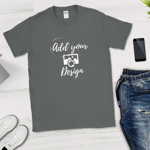 May include: A dark gray t-shirt with the text "Add your Design" in white lettering and a gold circle around the word "Add". A white image of a picture with a refresh arrow is inside the circle.