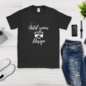 May include: Black t-shirt with a white circle and the text "Add your Design" inside the circle. The circle has a gold outline. A white image of a camera with a refresh arrow is below the text.