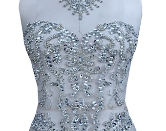 May include: A silver rhinestone applique with a floral design. The applique is on a white background and is perfect for adding sparkle to clothing or crafts.