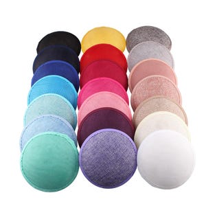 Op de afbeelding: Een verzameling kleurrijke, ronde stoffen hoedenbases in diverse tinten, waaronder zwart, geel, rood, roze en blauw. De bases zijn in nette rijen gerangschikt en tonen een verscheidenheid aan texturen en tinten, perfect voor hoedenmakerij.