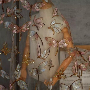May include: A sheer fabric with a delicate pattern of iridescent butterflies. The butterflies are embroidered with sequins and have a pink, gold, and silver color scheme.