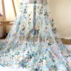以下が含まれることがあります： カラフルな花の刺繍が施されたシアー生地。繊細な素材は、青、ピンク、黄色、緑の色合いの花を様々に使用し、鮮やかで複雑なデザインを作り出しています。ドレス、ベール、その他の装飾品に最適です。