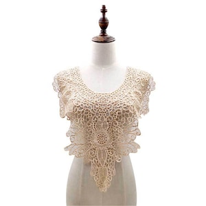 May include: A delicate, cream-colored lace collar with a scalloped edge and a floral design. The lace is intricate and detailed, with a central flower motif.