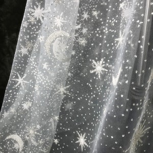 May include: White sheer fabric with a celestial design. The fabric features embroidered stars, moons, and scattered silver glitter, creating a shimmering, starry night effect. Ideal for crafting or decorative purposes.
