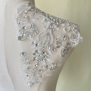 May include: A delicate white lace applique with a floral design embellished with clear rhinestones. The applique is perfect for adding a touch of sparkle to a wedding dress or other special occasion garment.