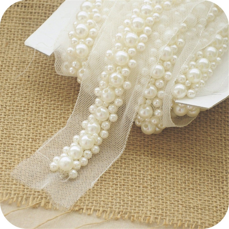 Op de afbeelding: Witte pareltrim met een delicate mesh-rug. De trim is opgerold op een witte kaart.