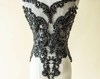 May include: A black beaded lace applique with a delicate floral design. The applique is perfect for adding a touch of elegance to any garment.