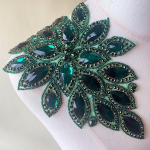Peut inclure: Une applique en strass verte avec un motif floral. L'applique est faite de petits strass facetés et est parfaite pour ajouter une touche d'éclat à n'importe quel vêtement.