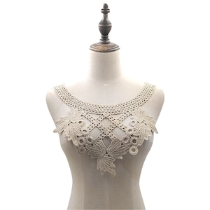 May include: Beige lace applique with a floral and geometric design. The lace is displayed on a mannequin, showcasing the intricate details of the embroidery. This decorative lace is suitable for various sewing and craft projects.