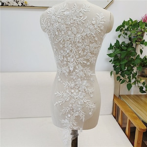 May include: White beaded lace applique with floral and leaf designs. The applique is on a mesh backing and is ideal for adding a touch of elegance to any garment.