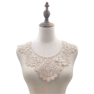 May include: A delicate, off-white lace collar with a scalloped edge. The collar is displayed on a white mannequin.