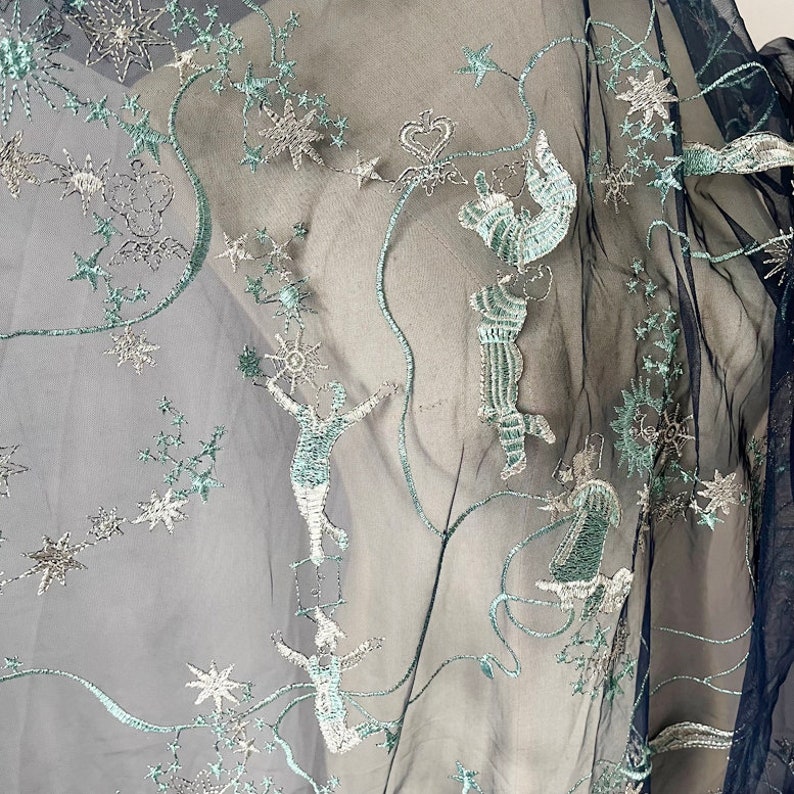May include: Black sheer fabric with silver and teal embroidery of stars and figures. The fabric has a delicate, airy feel.