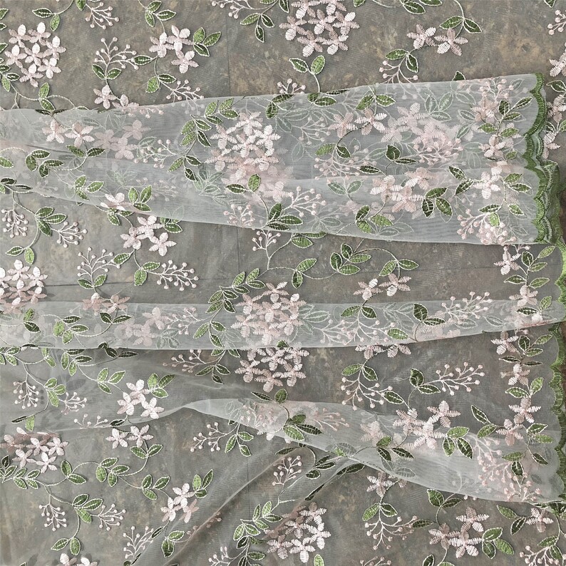 May include: White sheer fabric with a delicate floral embroidery pattern. The flowers are pink and the leaves are green.