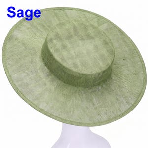 Peut inclure: Un chapeau vert sauge à larges bords avec une calotte plate et une texture tissée semi-transparente. Le mot Sage est imprimé en bleu dans le coin supérieur gauche. Le chapeau présente un bord circulaire structuré et une calotte cylindrique.