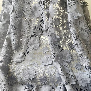 Pode incluir: Tecido de renda cinza com um delicado padrão floral. O tecido é feito de um material macio e leve e tem uma sensação delicada e feminina.