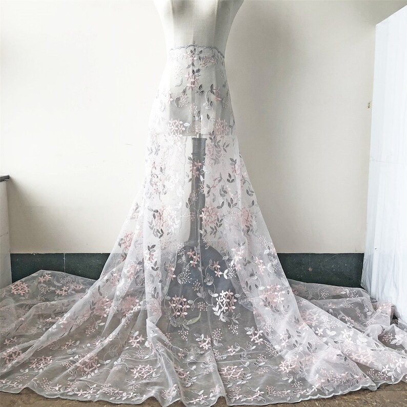 May include: White tulle fabric with embroidered pink and gray floral designs. The fabric is draped over a dress form.