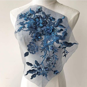 Può includere: Un'applicazione floreale blu con accenti di perle su un tessuto di rete trasparente. L'applicazione presenta intricati disegni floreali e perline delicate.