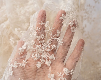 May include: Close-up of ivory lace fabric with a delicate floral pattern. The lace is sheer and has a soft, romantic feel.