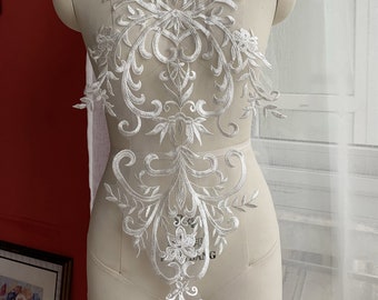 May include: White lace applique with a floral and scroll design. The lace is delicate and intricate, and would be perfect for adding a touch of elegance to a wedding dress, bridal gown, or other special occasion garment.