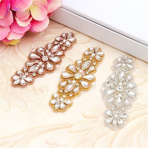 Może przedstawiać: Trzy ozdoby z kryształków w kolorze złotym, srebrnym i różowym złocie. Każda ozdoba zawiera skupisko przezroczystych kryształków i pereł w kwiatowym wzorze.