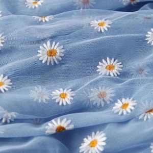 Könnte beinhalten: Hellblauer, durchsichtiger Stoff mit weißer Gänseblümchen-Stickerei.