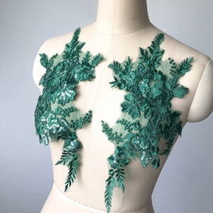May include: Two green floral lace appliques with sequins. The appliques are on a white background and are perfect for adding a touch of elegance to any project.