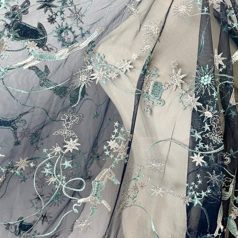 May include: Black sheer fabric with silver and teal embroidery of stars, moons, and other celestial designs.
