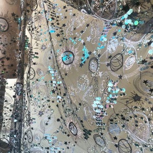 Puede incluir: Tela negra transparente con lentejuelas plateadas y turquesa y bordados de estrellas, lunas y remolinos.