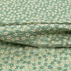 May include: A close-up of a teal fabric with a white floral pattern. The fabric has a textured, raised surface.