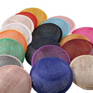 Op de afbeelding: Een verzameling kleurrijke, ronde hoedenbases in verschillende tinten, waaronder roze, blauw, geel en groen. De hoedenbases hebben een geweven textuur en zijn in een gelaagde opstelling gerangschikt. De randen zijn netjes afgewerkt, wat een elegante uitstraling geeft.