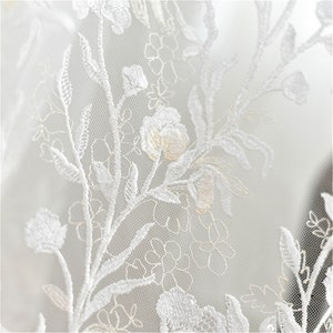 May include: White lace fabric with a delicate floral pattern. The fabric is sheer and has a soft, romantic feel.