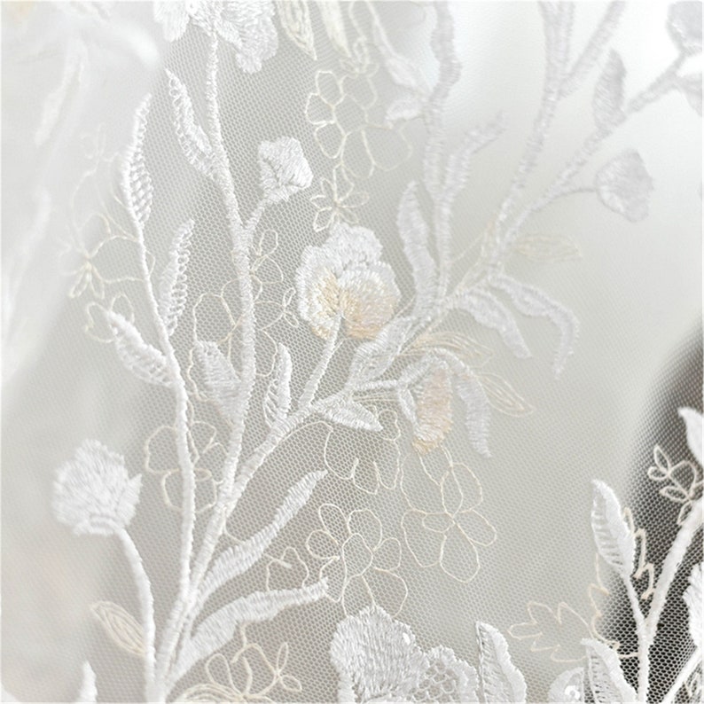 May include: White lace fabric with a delicate floral pattern. The fabric is sheer and has a soft, romantic feel.