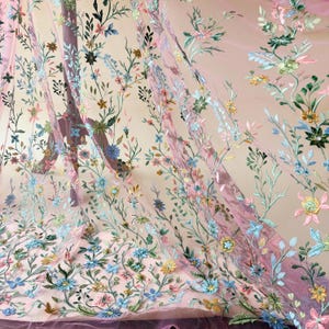 May include: Sheer pink fabric with embroidered floral patterns. The embroidery features a variety of colorful flowers in shades of blue, yellow, green, and pink, with delicate green stems and leaves. The fabric is lightweight and flowing, ideal for apparel or decorative projects.