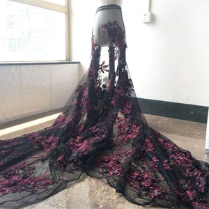 May include: Black and burgundy floral lace fabric with 3D embellishments. The lace is delicate and intricate, with a soft, flowing texture.