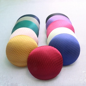 Puede incluir: Una colección de bases de sombreros redondos y coloridos en varios tonos, incluyendo dorado, rojo y azul. Cada base está cubierta con una red a juego, creando una apariencia texturizada. Los sombreros están dispuestos en filas ordenadas, mostrando una variedad de colores.