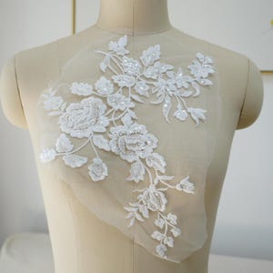 May include: White floral lace applique with beaded embellishments. The lace features delicate flowers and leaves, perfect for adding a touch of elegance to wedding dresses, bridal accessories, or other craft projects.