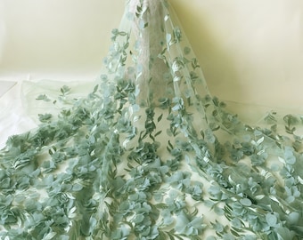 May include: Sage green floral lace fabric with 3D flowers. The fabric is sheer and delicate, with a soft, flowing texture.
