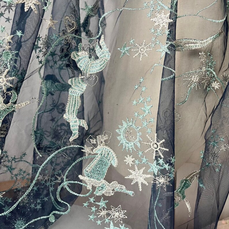 May include: Black sheer fabric with silver and teal embroidery of stars and whimsical figures.