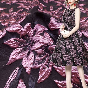 May include: A black fabric with a pink floral pattern. The fabric has a raised texture, giving it a 3D effect. The flowers are large and have a delicate, feminine look.