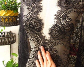 May include: Black lace fabric with a floral pattern. The lace has a scalloped edge and is sheer.