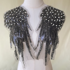 Puede incluir: Un par de aplicaciones negras de lentejuelas y cuentas con un diseño de flecos. Las aplicaciones están unidas a una tela de malla negra transparente.