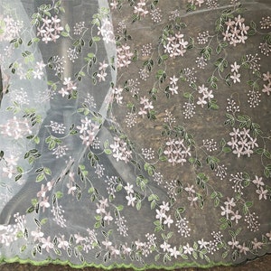 May include: White sheer fabric with a delicate floral embroidery pattern in pink and green. The fabric has a scalloped edge.
