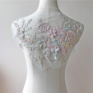 May include: A delicate floral applique with pastel pink, blue, and green flowers and leaves. The applique is made of lace and beads and is perfect for adding a touch of elegance to any garment.