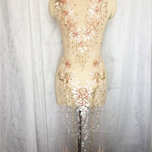 May include: A delicate lace applique with floral and leaf designs, embellished with pearls and beads in shades of gold, white, and pink. The applique features a cascading design with a pointed top and a flowing bottom.