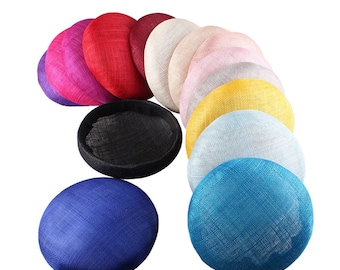 May include: A set of 11 round, flat, fabric hats in various colors, including pink, yellow, blue, black, and white. The hats are arranged in a semi-circle.