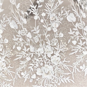 May include: White floral lace fabric with a delicate pattern of flowers and leaves. The lace is sheer and has a soft, romantic feel.