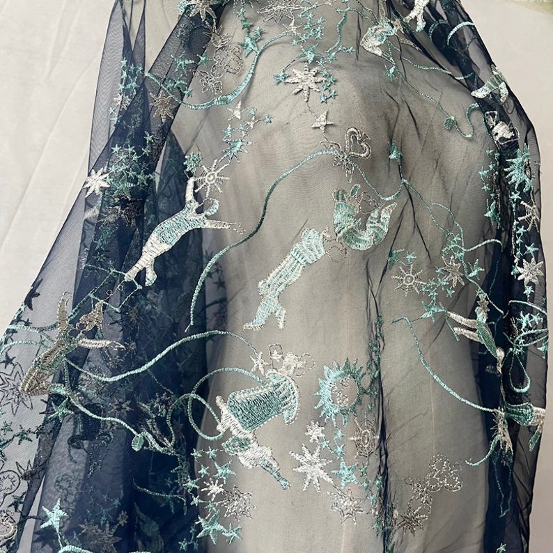 May include: Navy blue sheer fabric with silver and green embroidered stars, moons, and whimsical creatures.