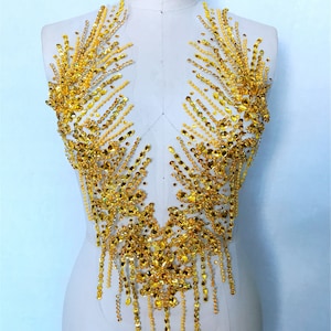 Peut inclure: Une embellissement pour vêtements en perles dorées et strass. L'embellissement est en forme de V et a un design en cascade.